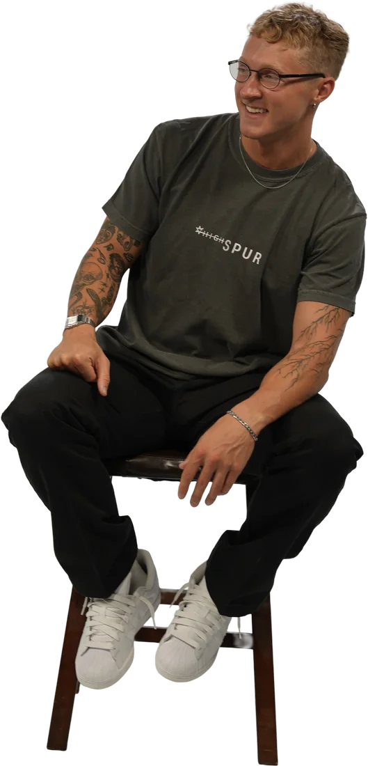 Benton Jackson seated on a wooden stool, smiling, in a charcoal T-shirt